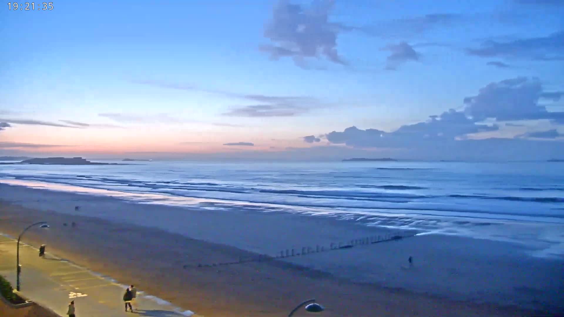 A wide, sandy beach stretches out to a calm ocean under a twilight sky with light clouds.