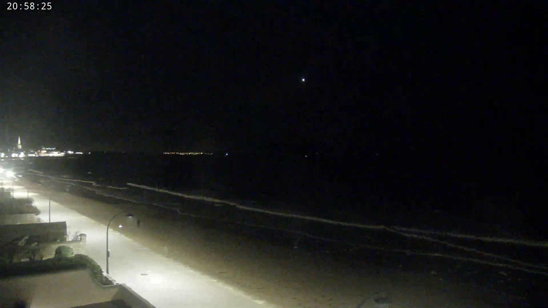 A nighttime view of a mostly empty beach with gently lapping waves under a clear, dark sky.