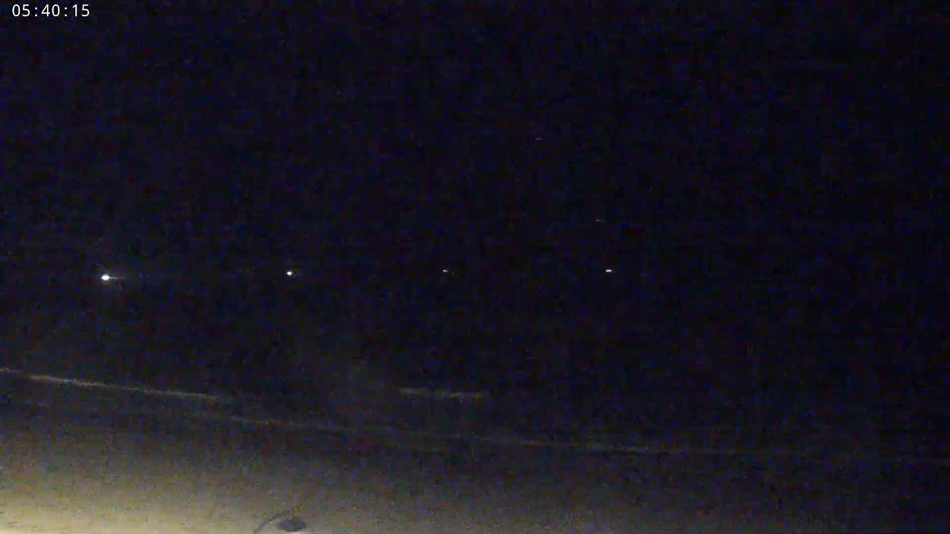 A dark beach at night is visible under a clear, starlit sky, with faint lights in the distance.