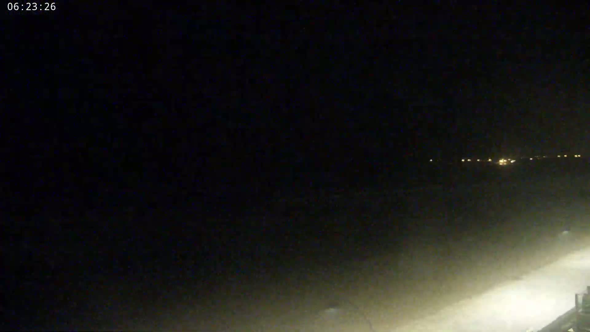 A dark, nighttime scene shows a hazy, light-colored area in the foreground and a line of distant lights on the horizon.