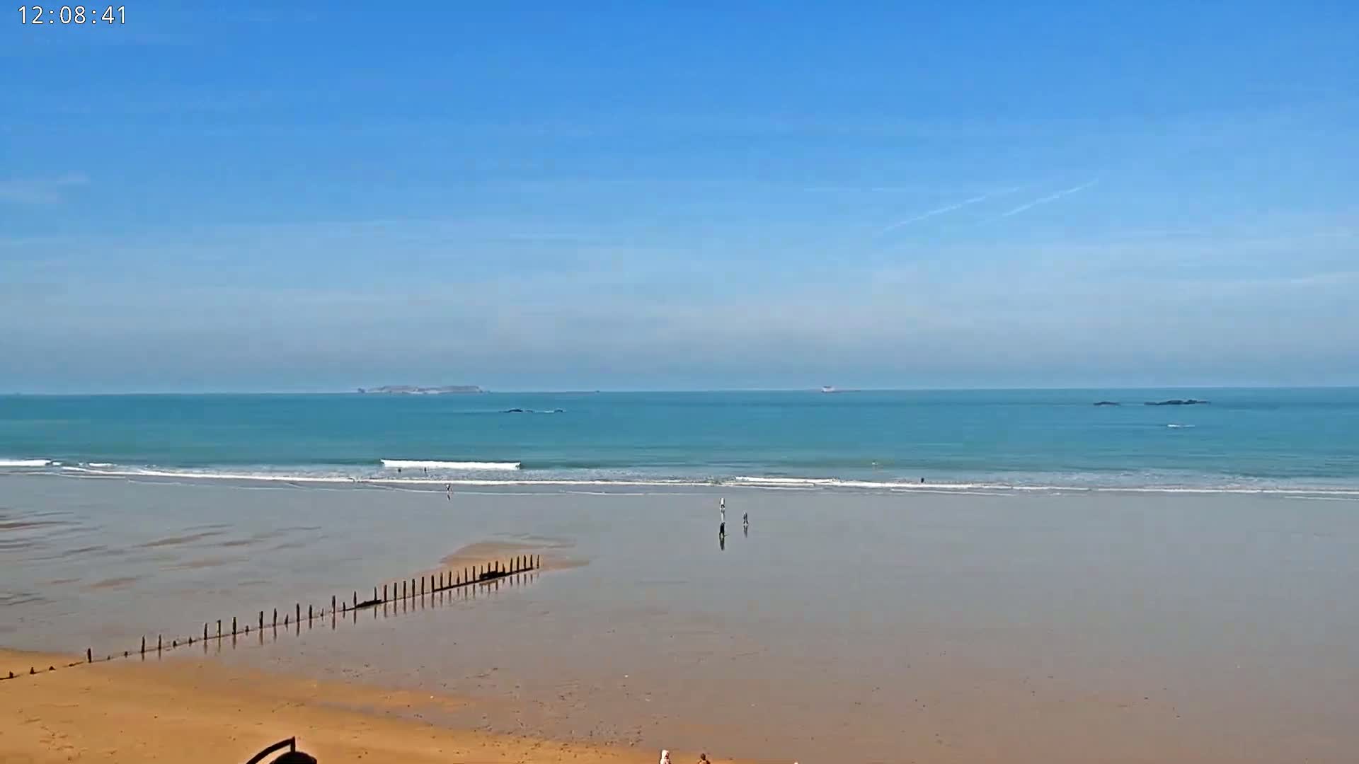 A sandy beach with calm, teal water and a few people is visible under a clear blue sky.