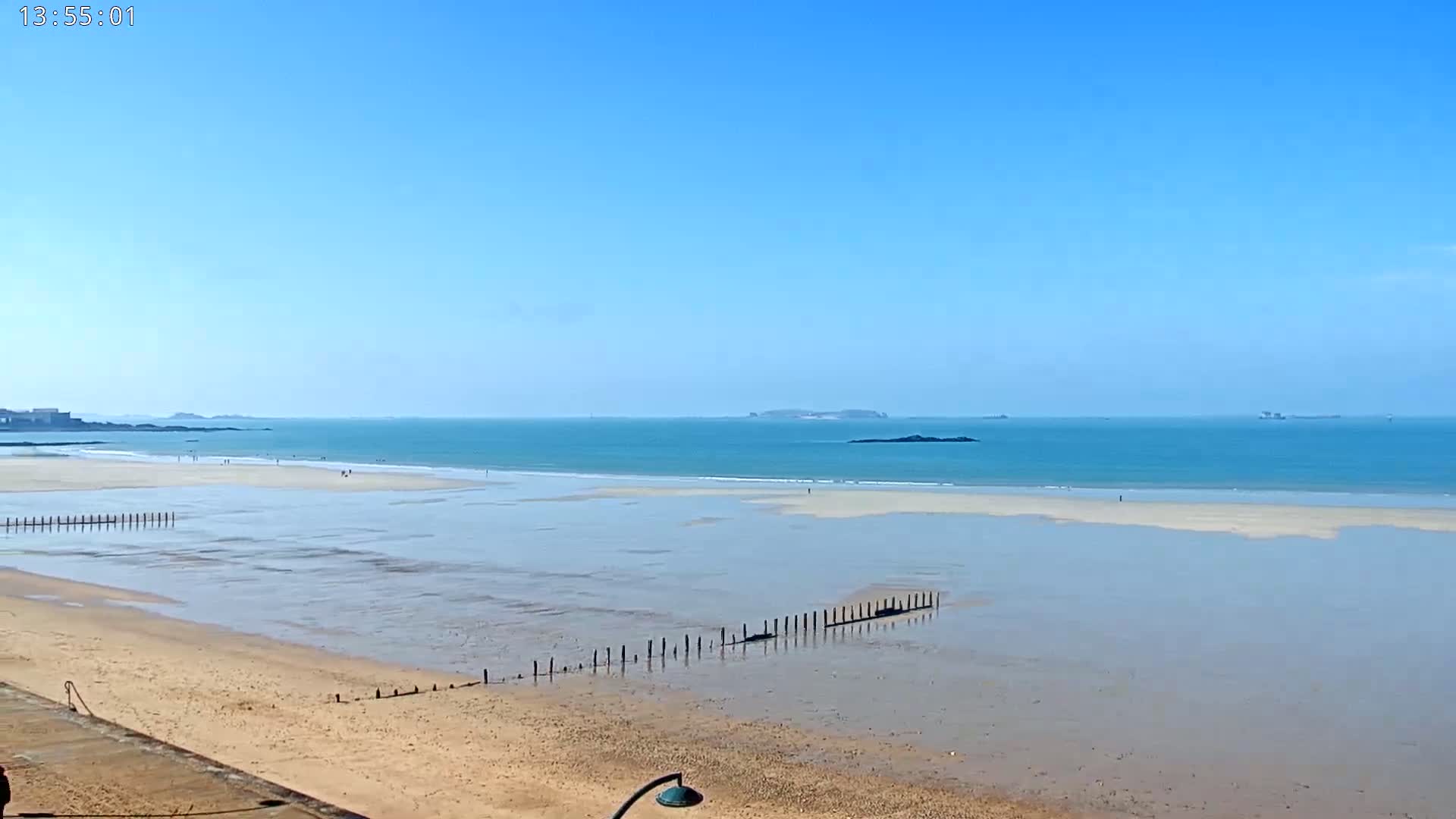 A sandy beach stretches to a calm, blue ocean under a clear, bright sky, with a few distant islands visible on the horizon.