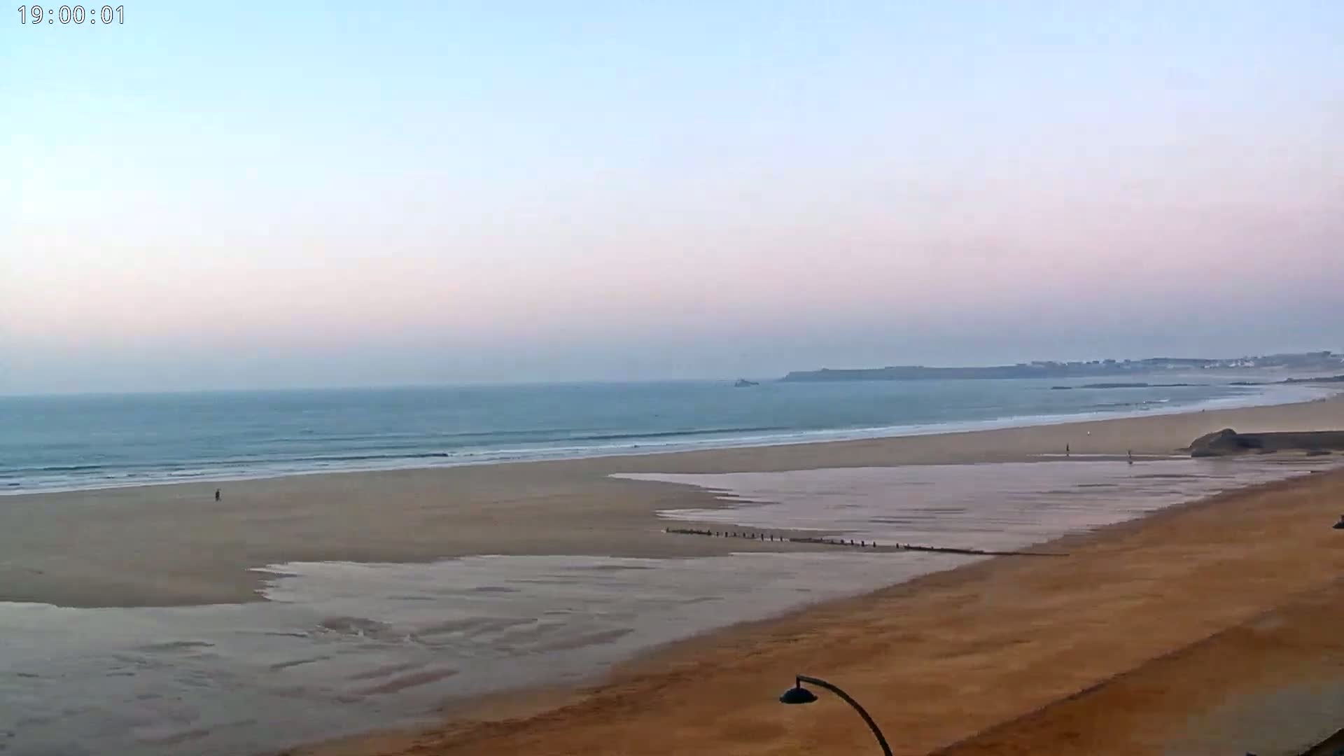 A wide, sandy beach with calm waves under a pale, dusk sky.