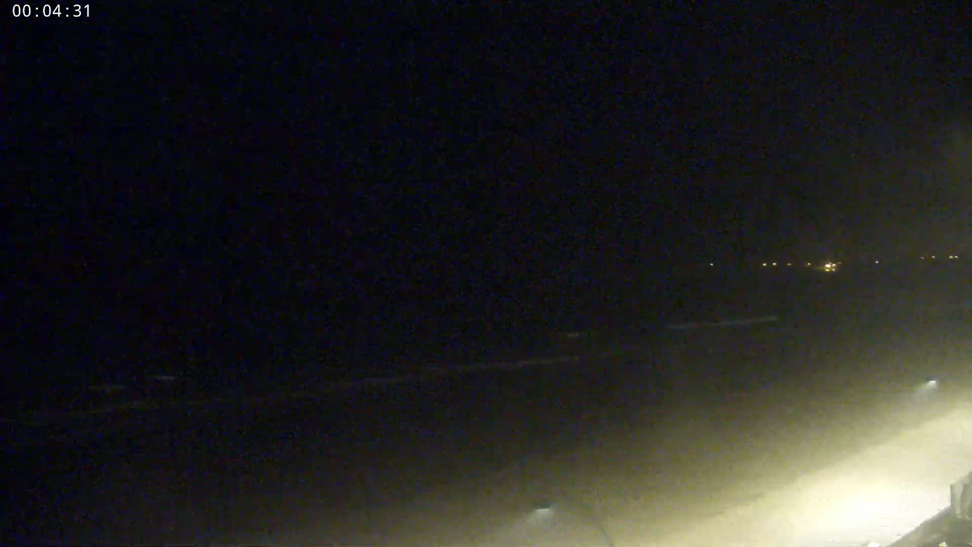 A nighttime, hazy view of a beach with faint waves and distant lights.