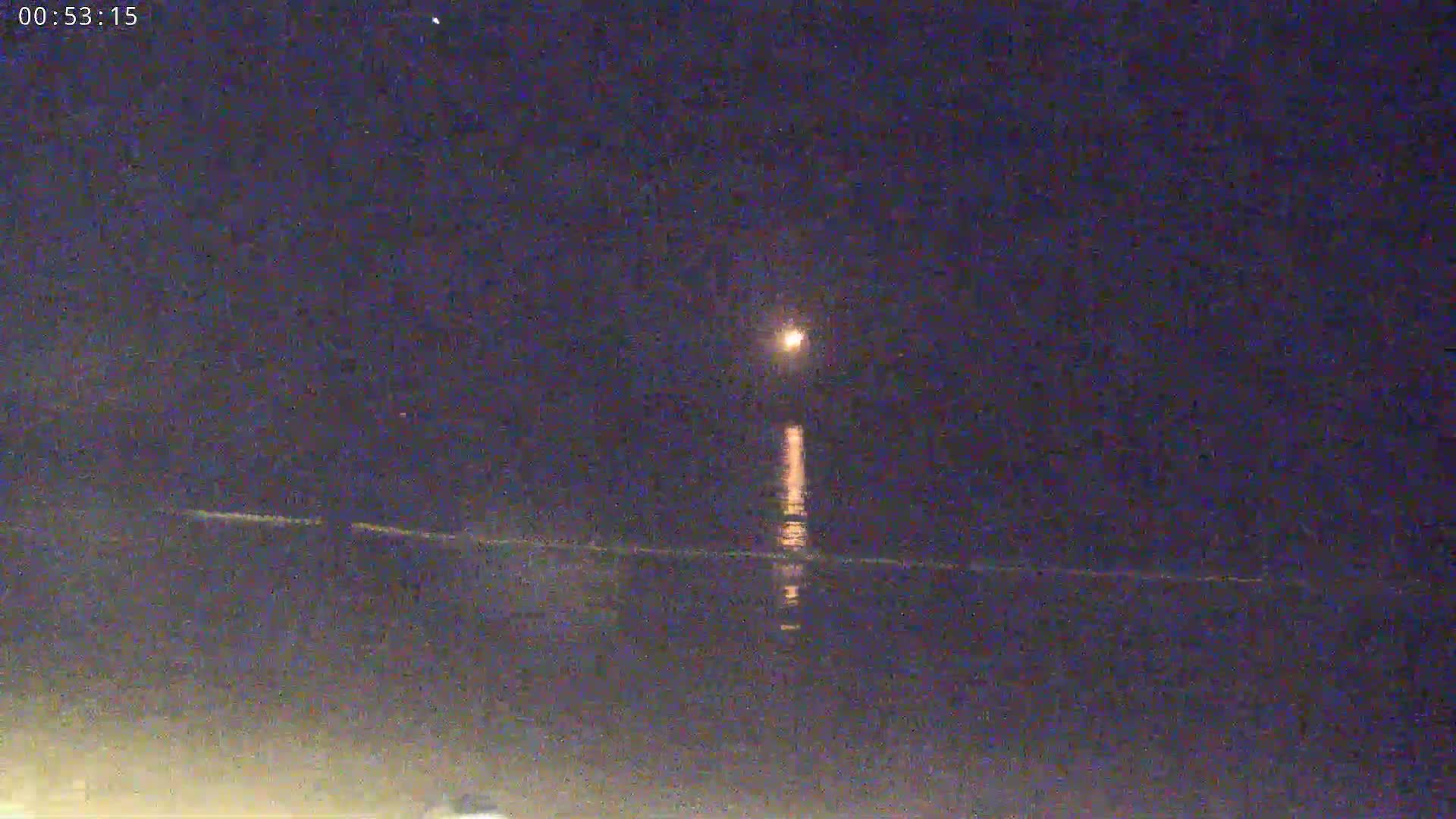 A bright moon shines over a dark, calm body of water at night.