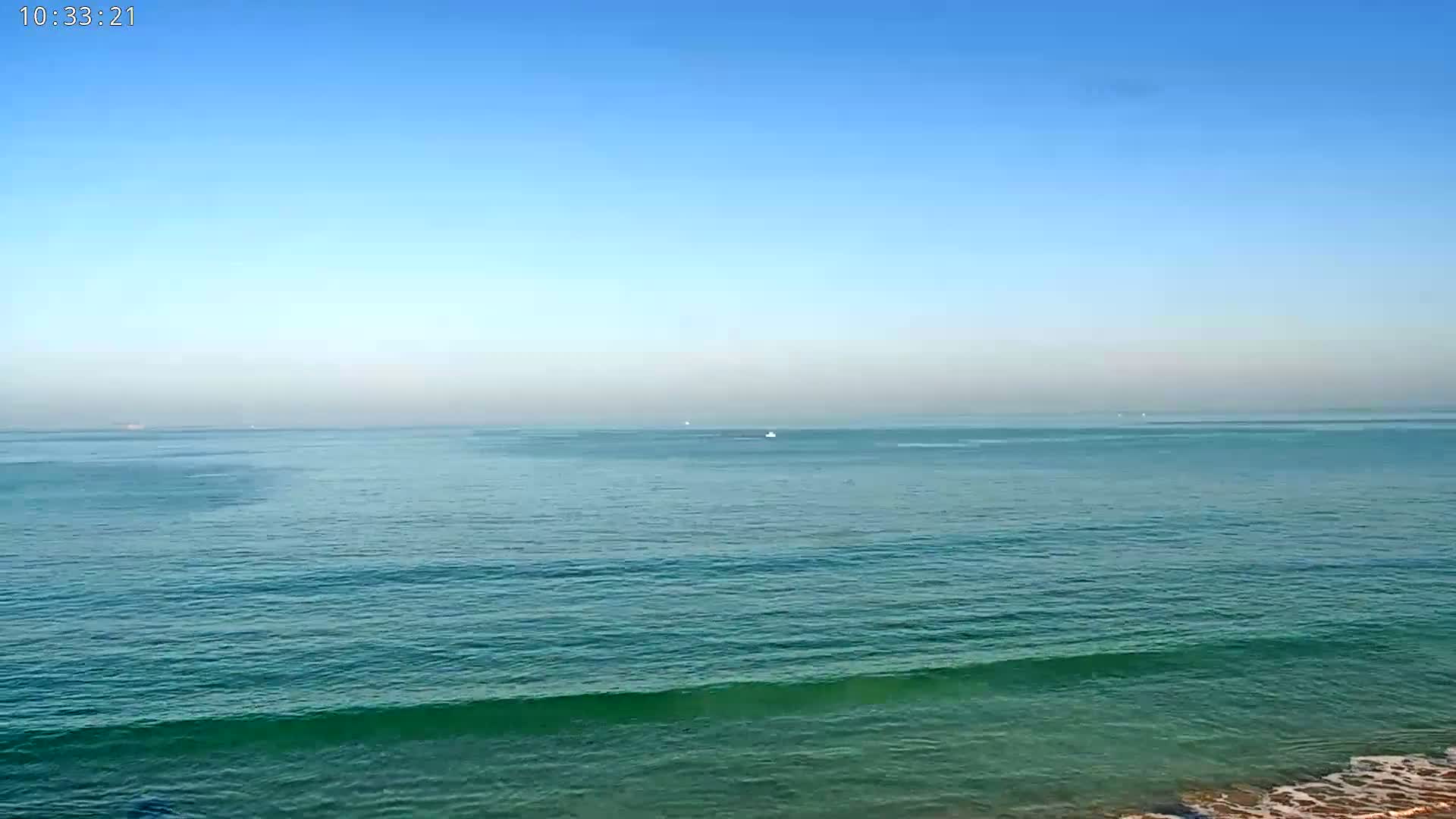 A calm, teal ocean stretches to a clear blue sky under sunny conditions.