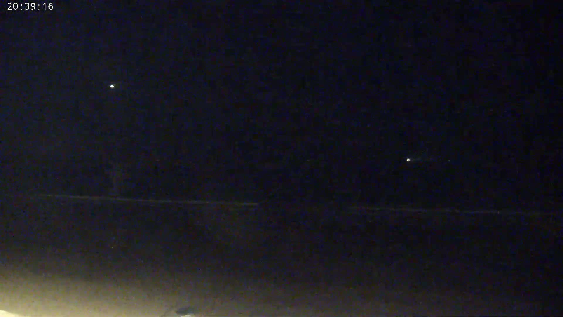 A dark, nighttime scene shows a few distant lights in the sky above a dark horizon.