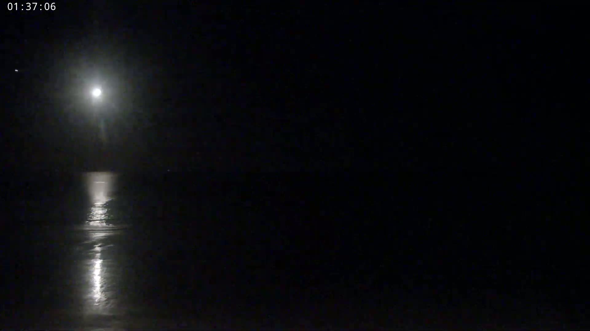 The image shows a bright moon illuminating a dark, calm body of water at night.