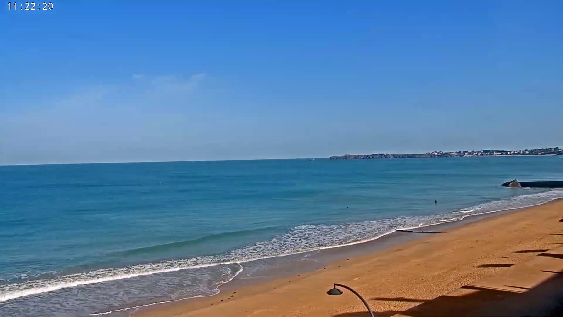 A sandy beach with gentle waves laps the shore under a clear blue sky.