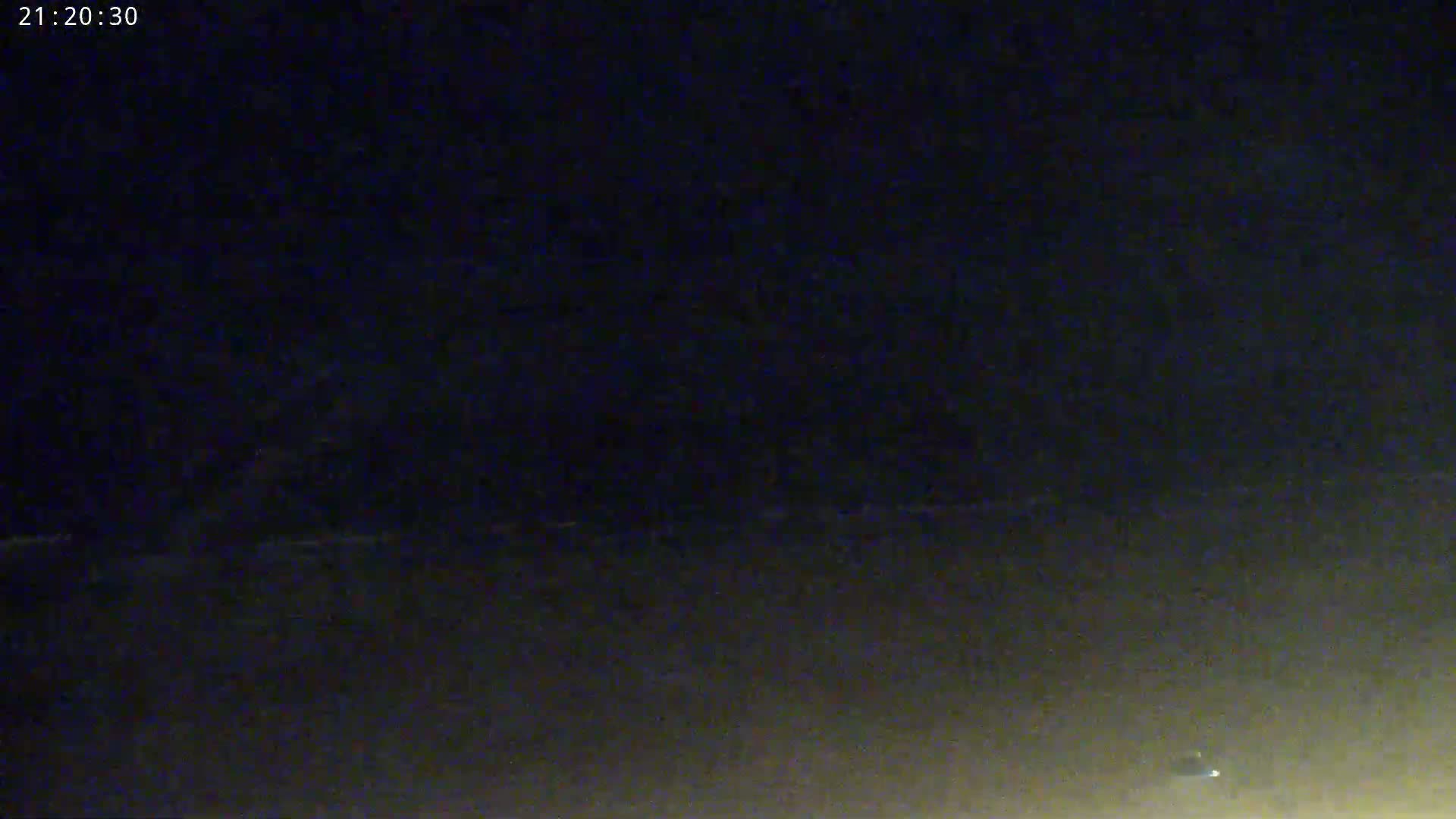 A dark, nighttime scene shows a dimly lit horizon line under a mostly clear sky.