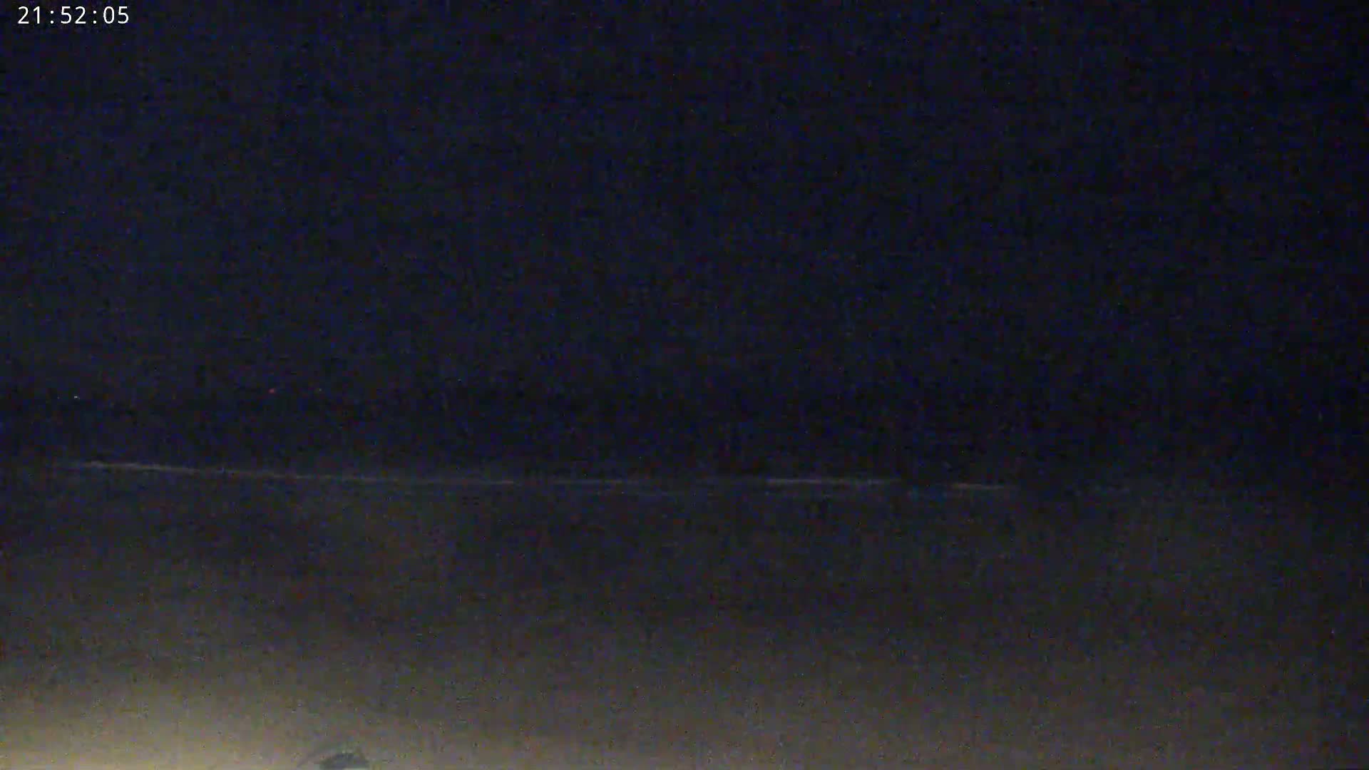 A dark, nighttime beach scene shows a mostly calm ocean under a clear, black sky.