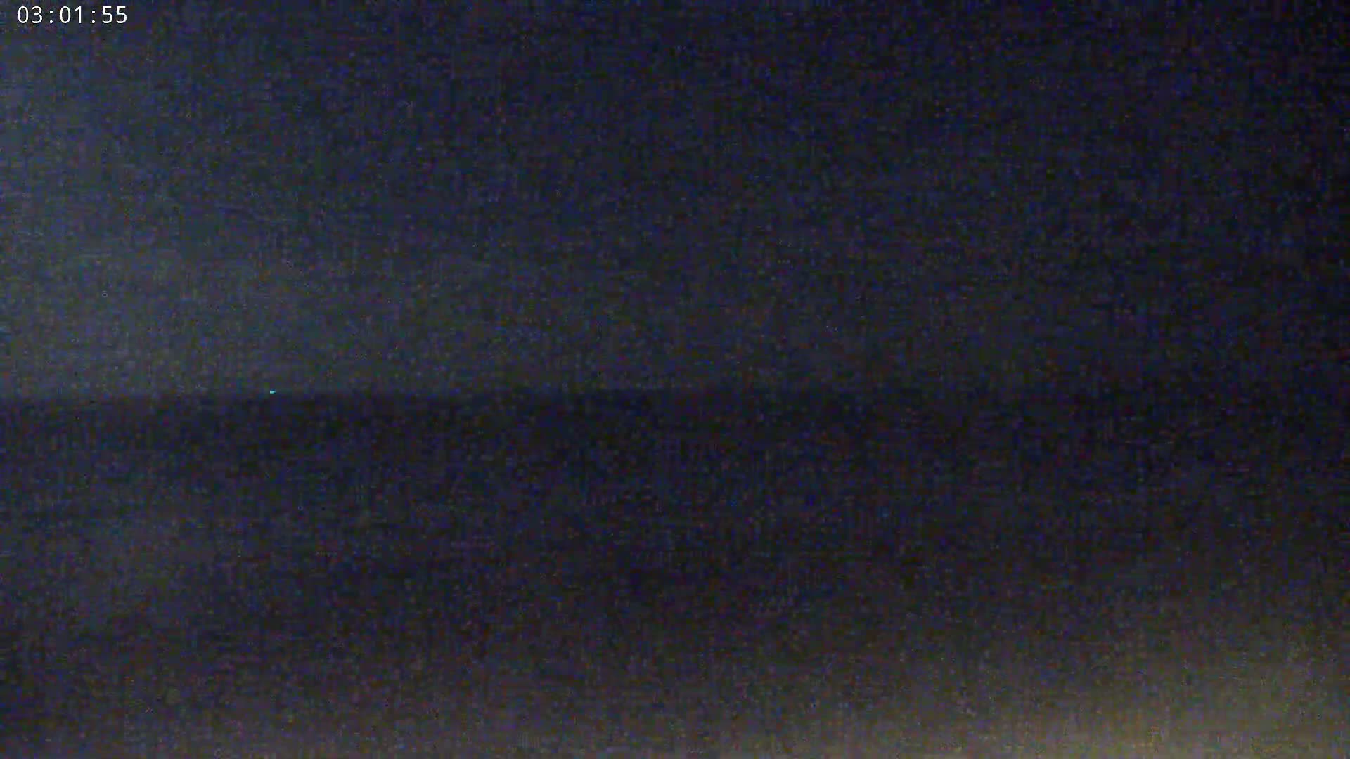 A dark, nighttime scene shows a mostly flat horizon line under a mostly clear, dark sky.