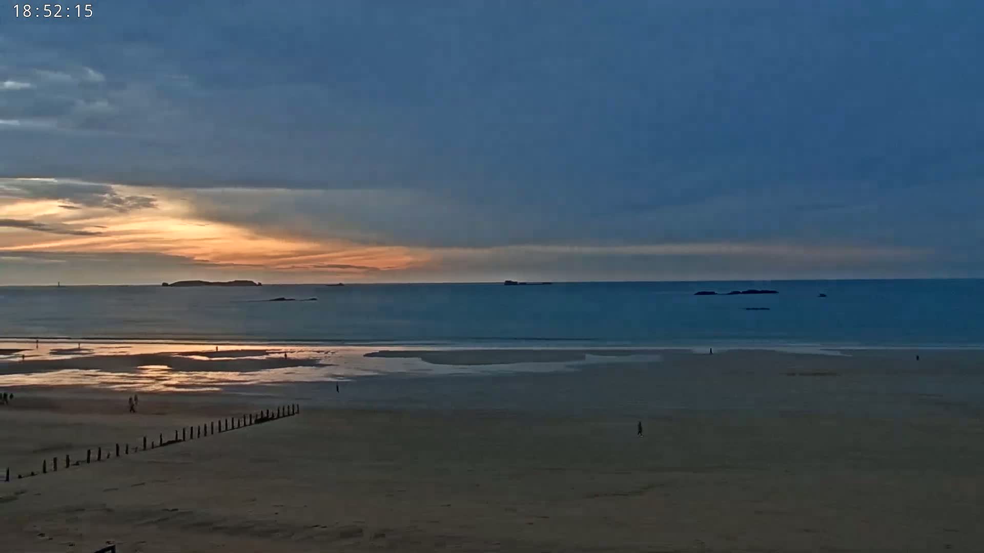 A wide sandy beach stretches out to a calm sea under a partly cloudy sunset sky.