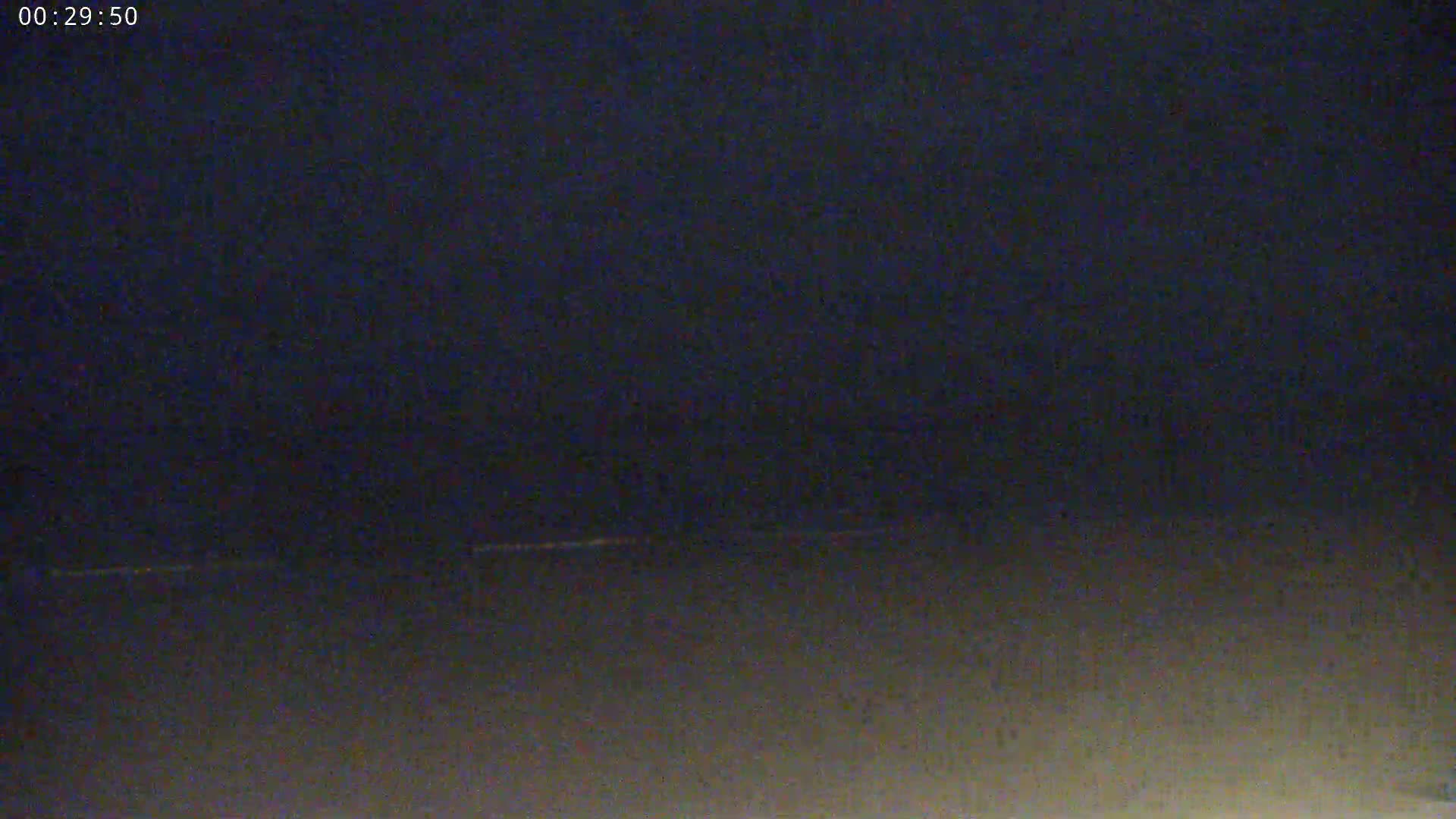 A dark, nighttime scene shows a faint line of lights on the horizon.