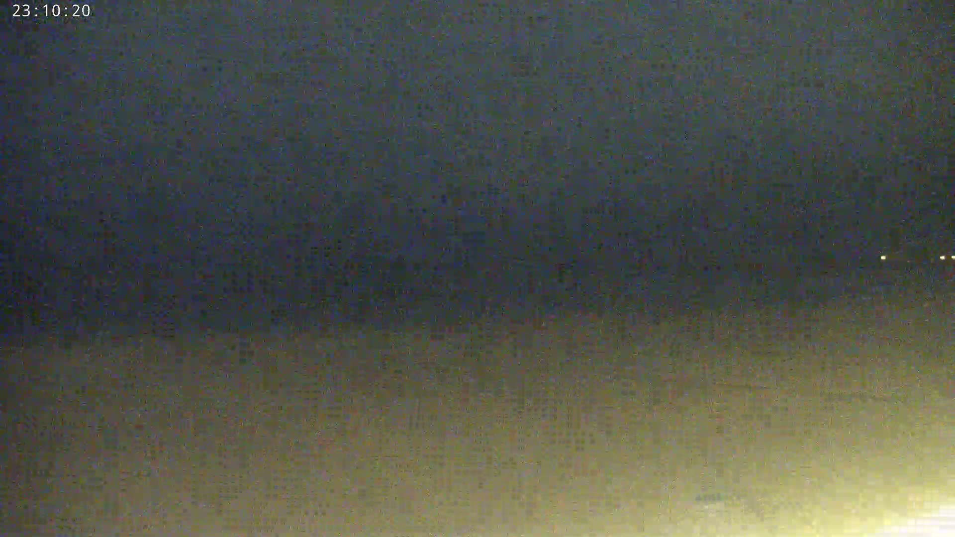 A dark, nighttime scene shows a dimly lit horizon with a few faint lights in the distance.