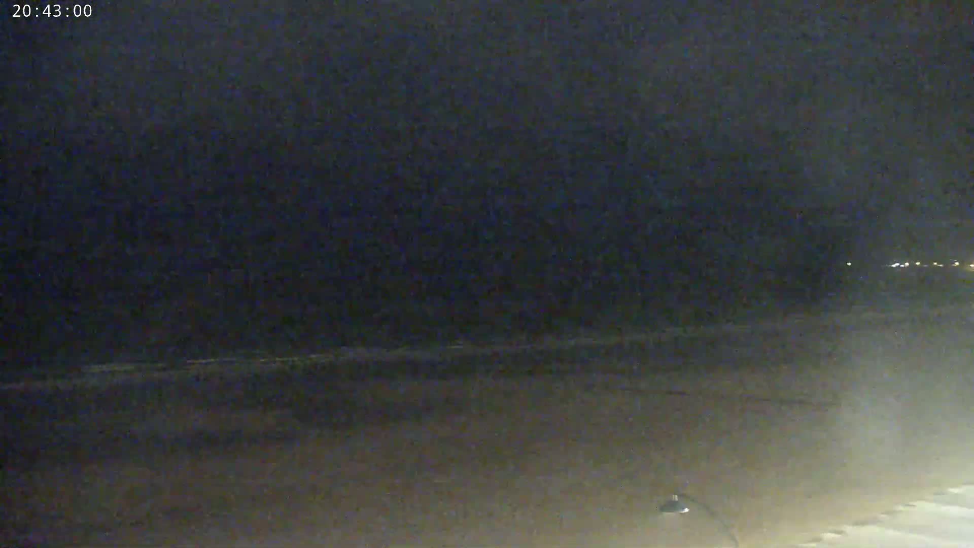 A dark, nighttime beach scene shows a mostly calm ocean under a clouded sky.