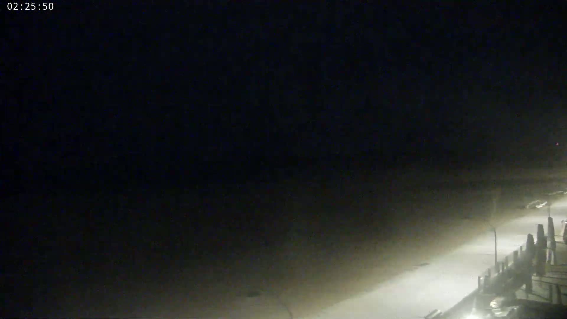A nighttime, foggy view of a beach and boardwalk.