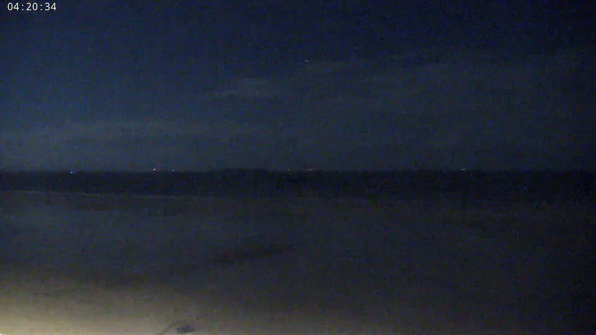 A dark, nighttime beach scene shows a calm ocean under a mostly clear sky.