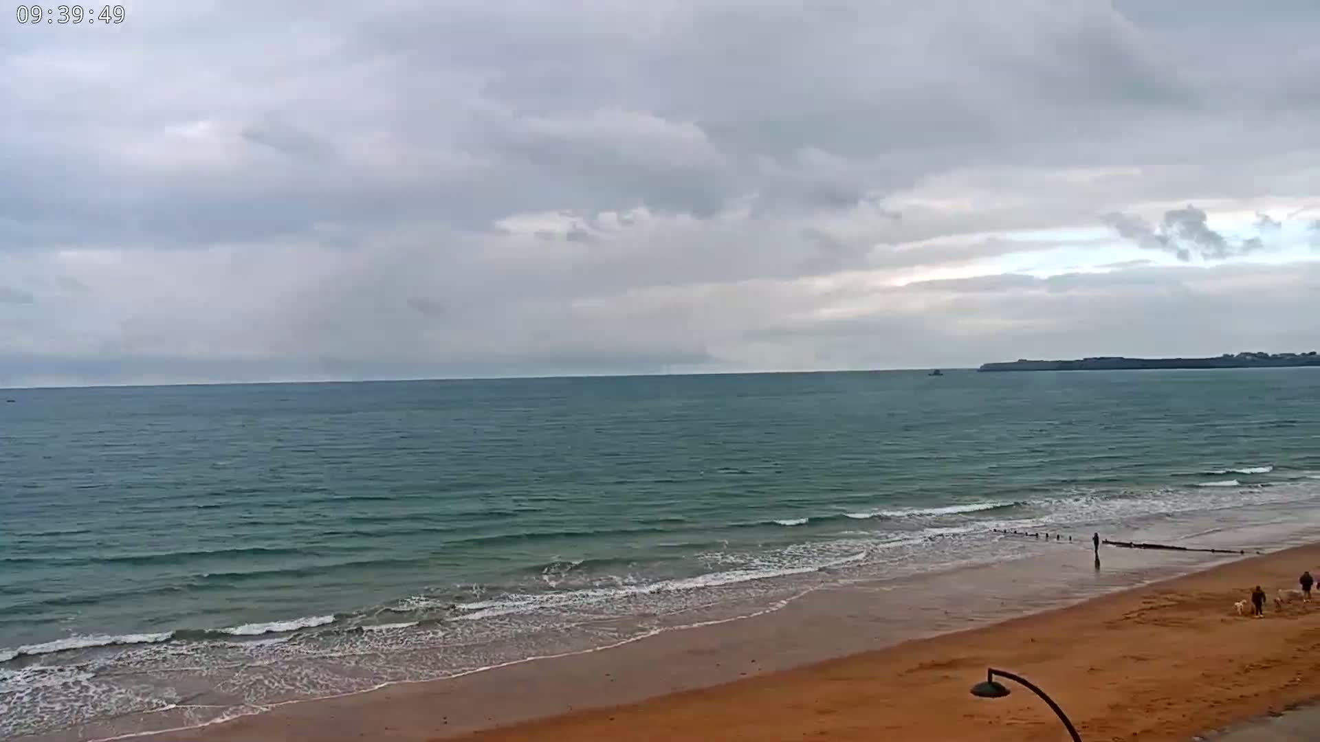 A sandy beach with gentle waves laps the shore under a cloudy sky.