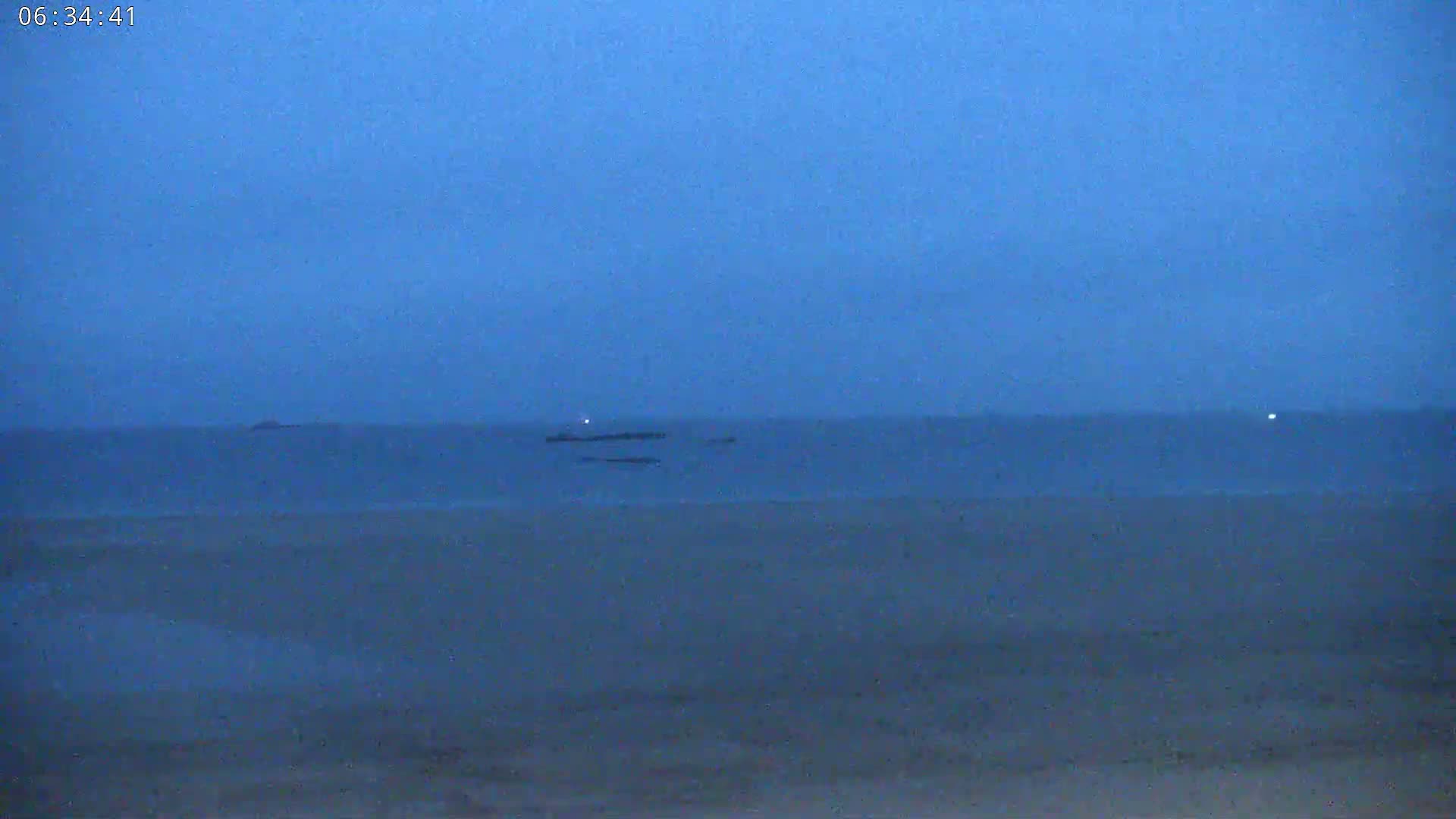 A dark, flat beach stretches to a calm, blue-grey sea under an overcast sky.