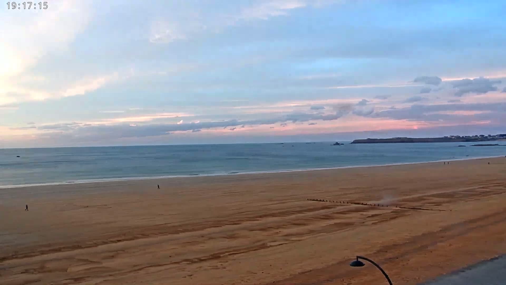 A wide sandy beach stretches to a calm ocean under a pale pink and blue sunset sky.