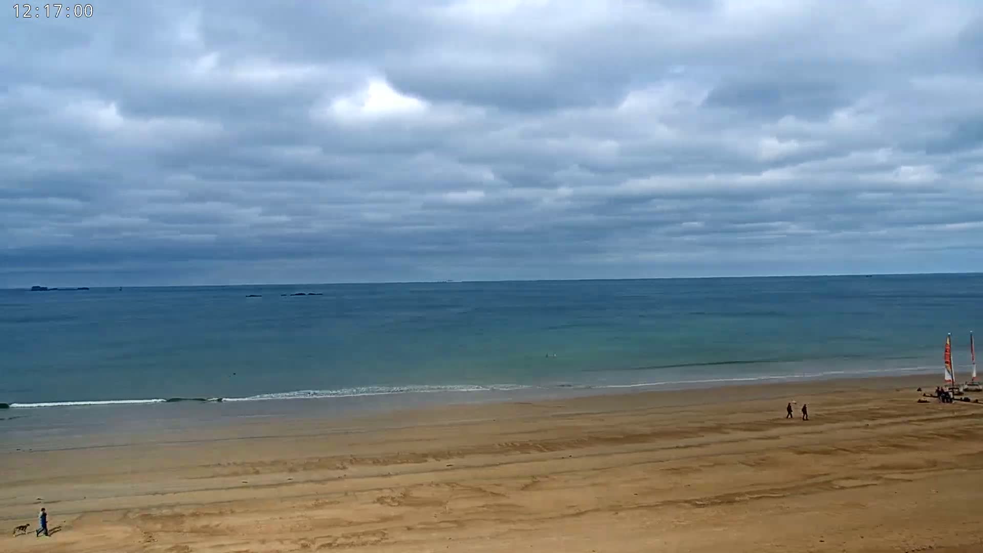 A wide sandy beach stretches to a calm ocean under a cloudy sky.