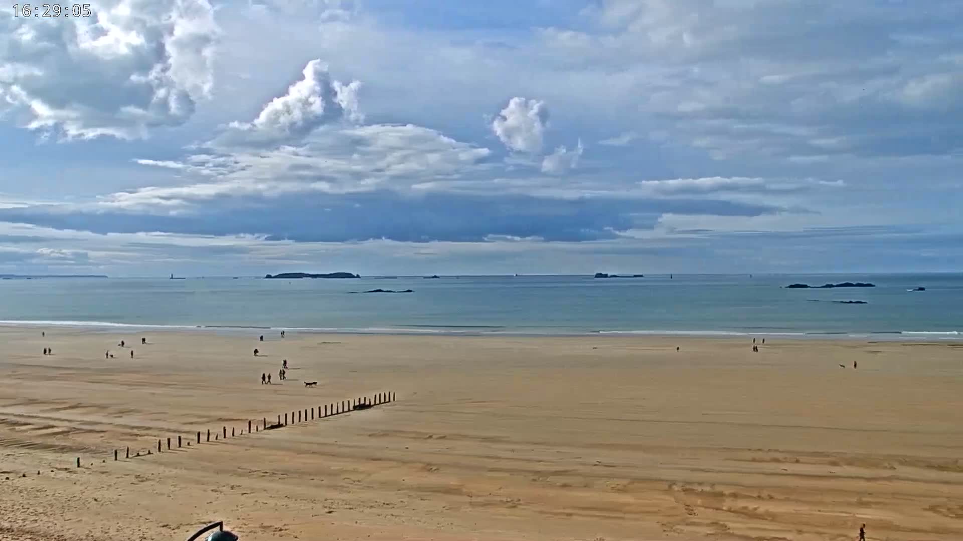 A wide sandy beach with scattered people stretches to a calm ocean under a partly cloudy sky.