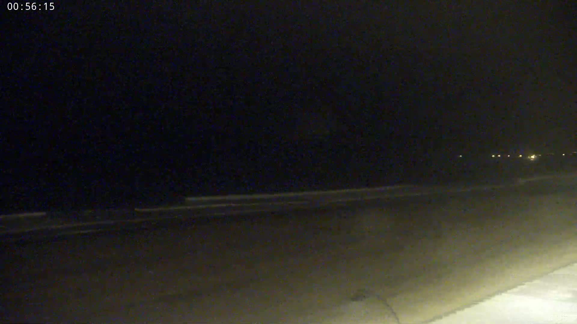A dark, nighttime scene shows a flat, empty road with faintly visible light sources in the distance.