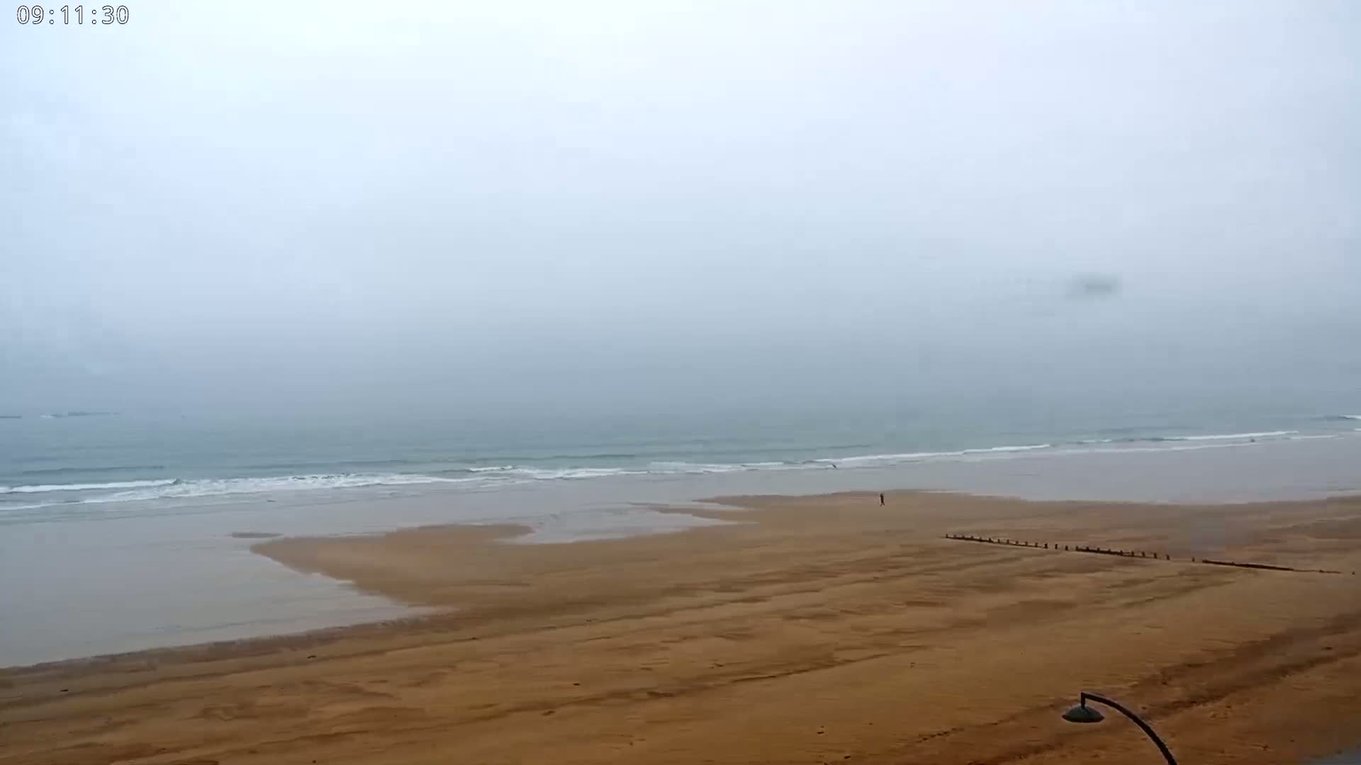 A wide, sandy beach stretches to a gray, foggy ocean with small waves.