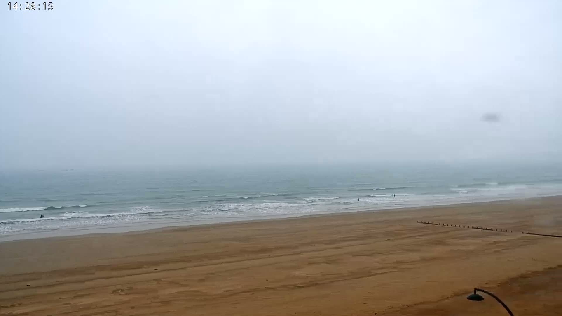 A wide sandy beach stretches to a misty ocean with small waves under an overcast sky.