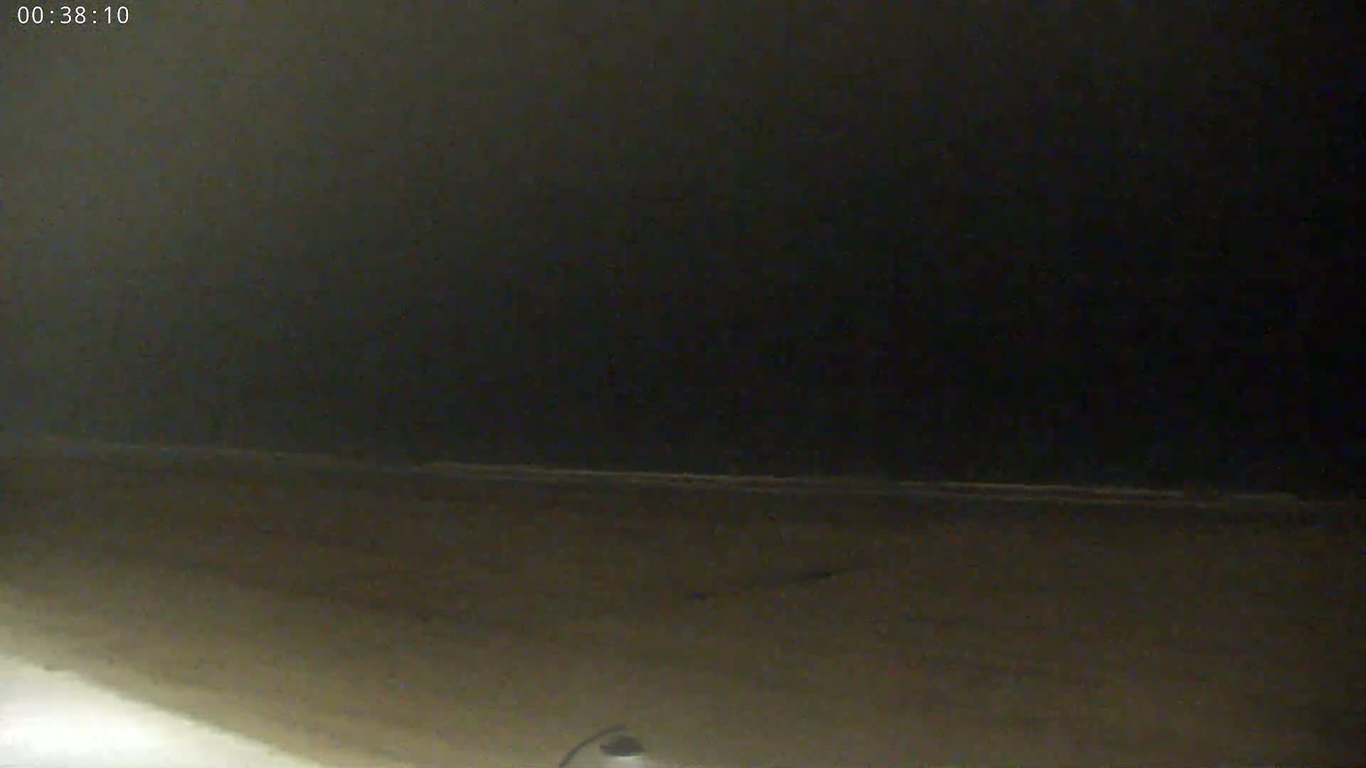 A dark, nighttime beach scene shows a dimly lit shoreline and a dark, mostly featureless sky.