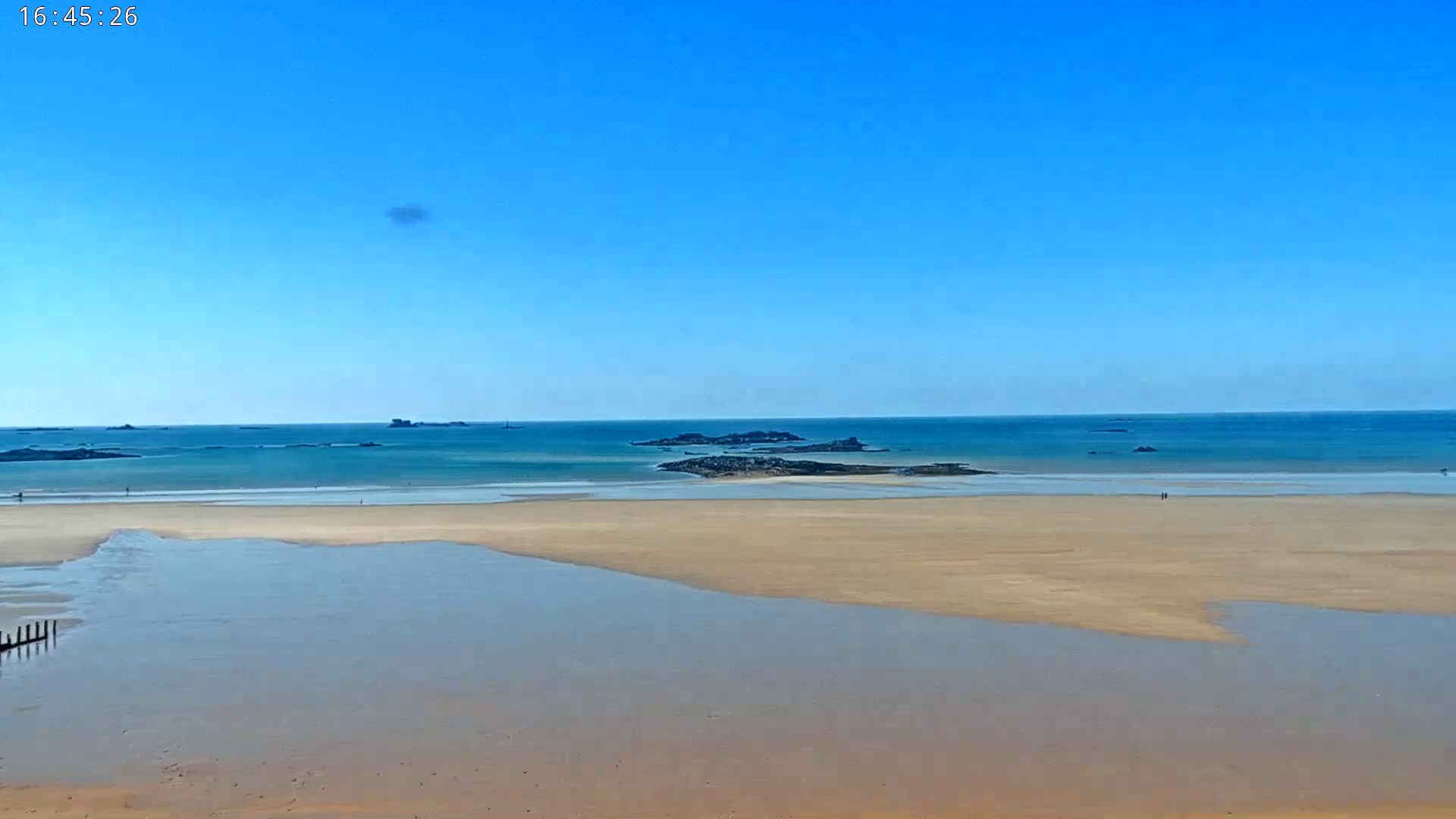 A sandy beach stretches out to a calm, teal ocean under a clear blue sky.