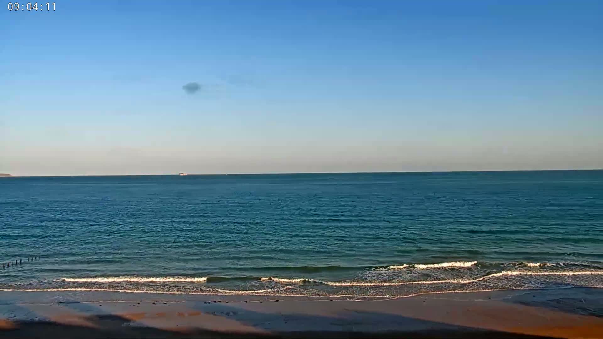A sandy beach with gentle waves laps the shore under a clear blue sky.