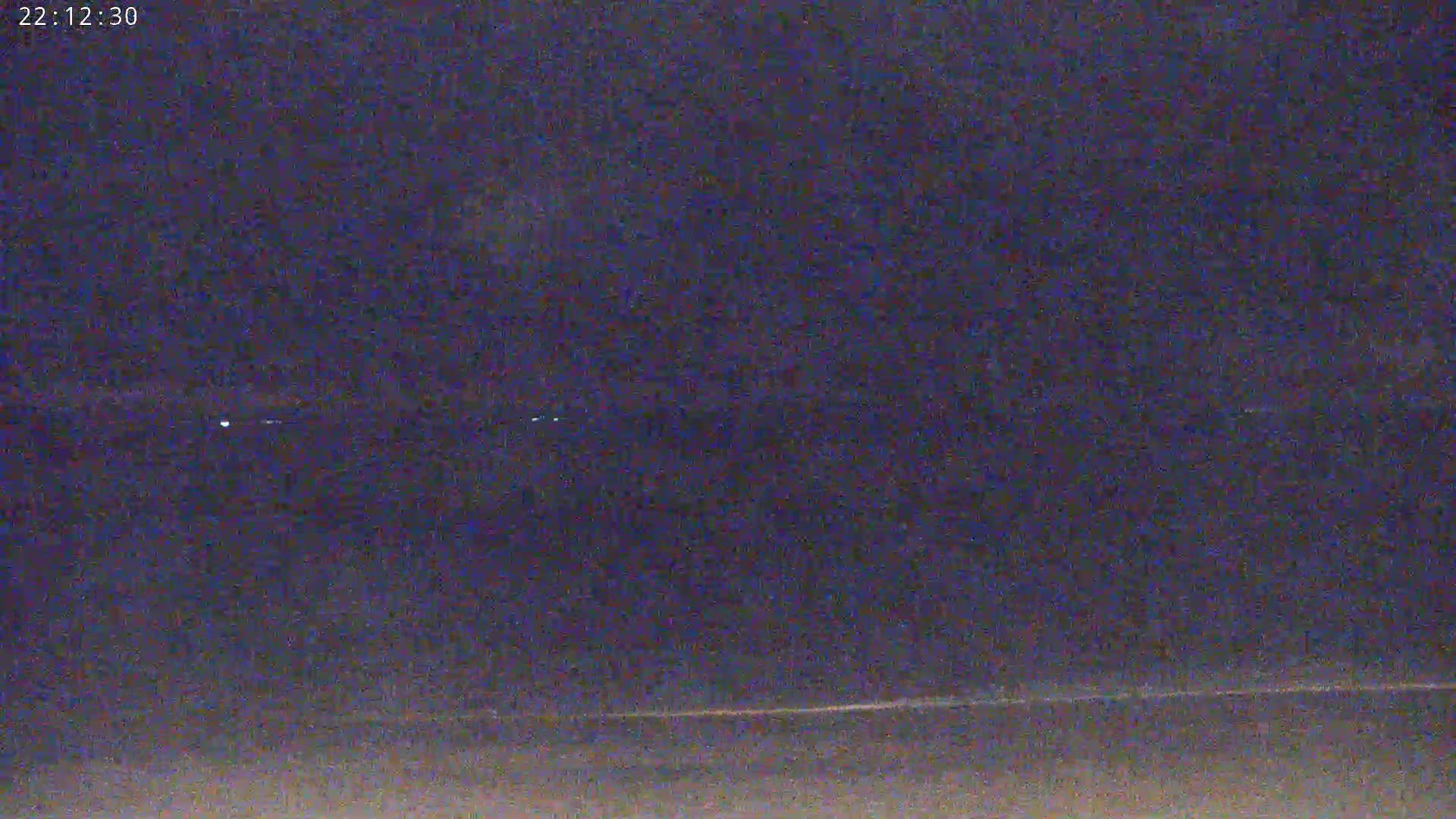A nighttime, low-light view shows a dark horizon line with a few faint lights in the distance.