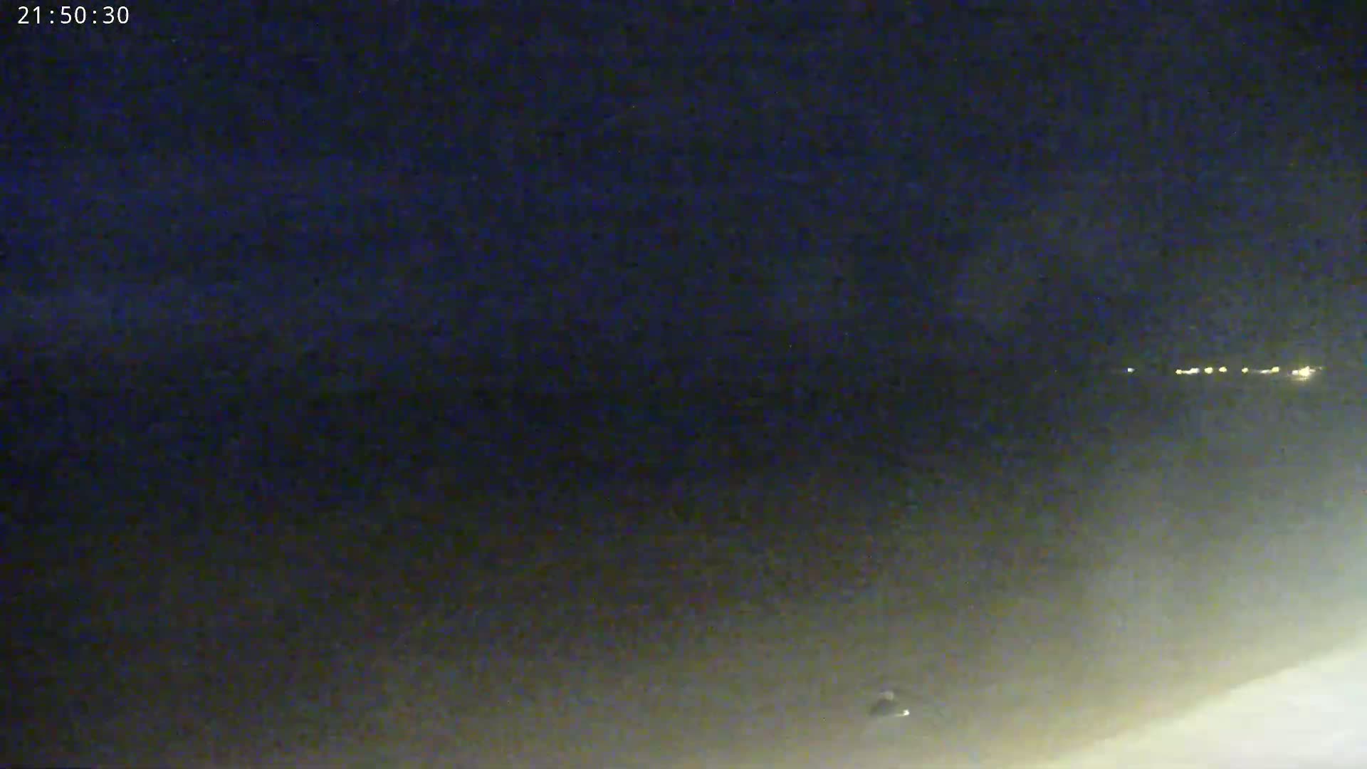 A nighttime, hazy or foggy scene shows a distant line of lights and a small object near the bottom.