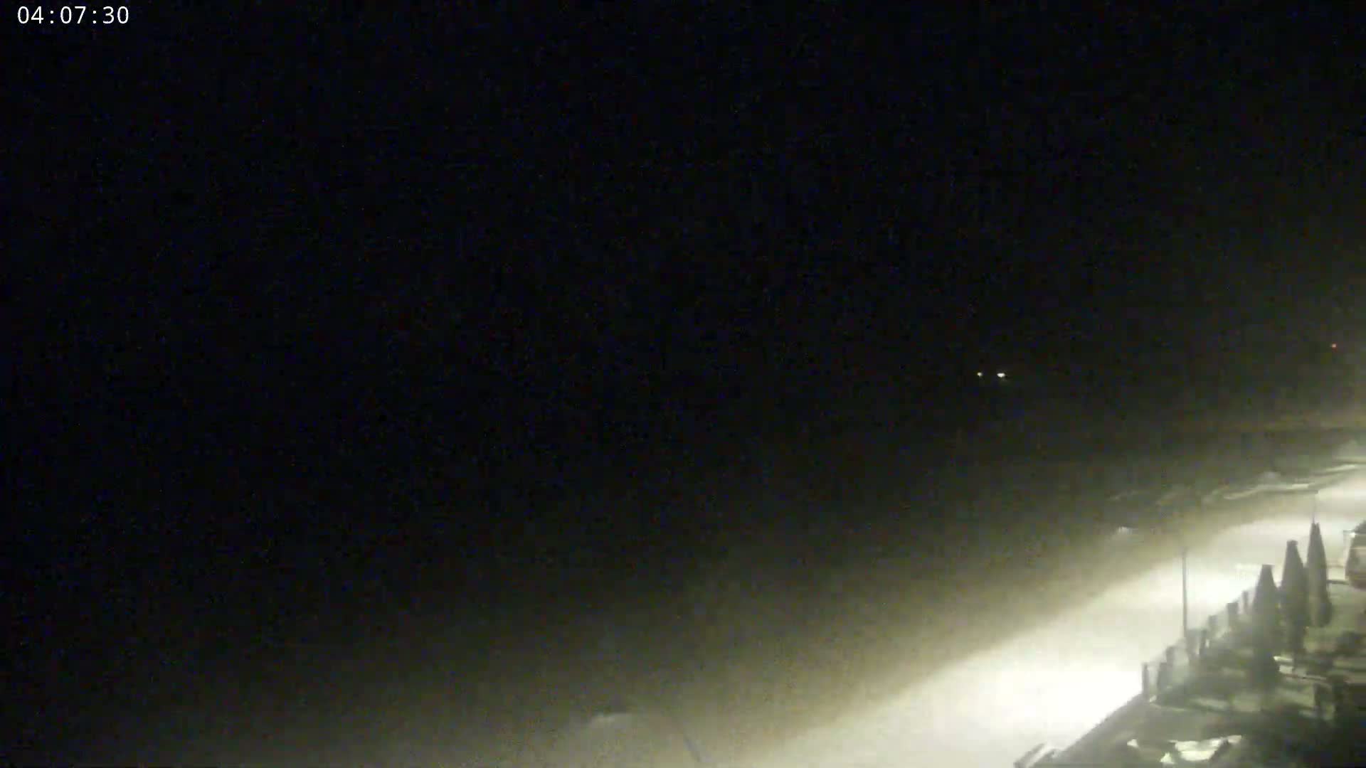 A nighttime view of a snow-covered beach with some structures visible in the lower right corner, under a dark sky.