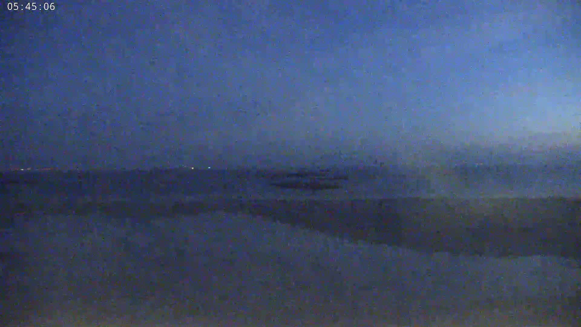 A hazy, dark blue landscape is visible at twilight, with a few distant lights faintly illuminating the scene.