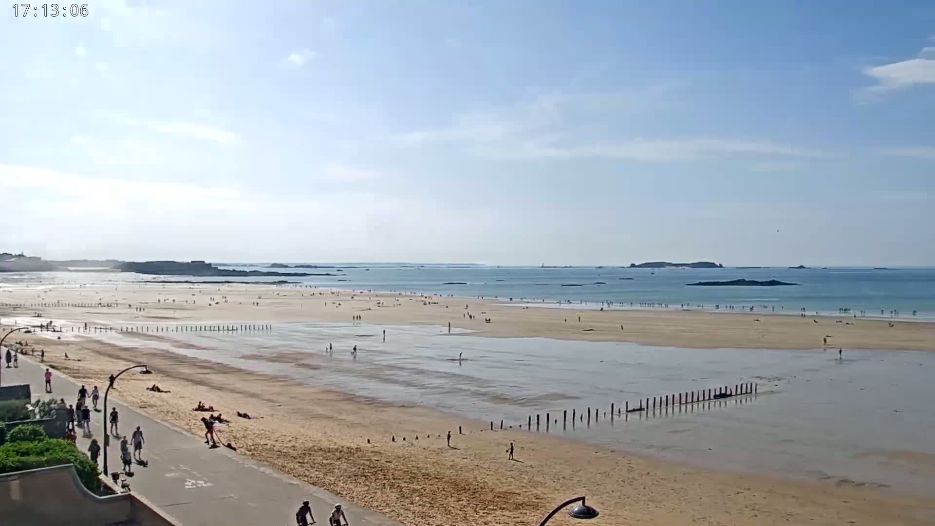 A sandy beach with many people on it stretches to a calm ocean under a mostly sunny sky.