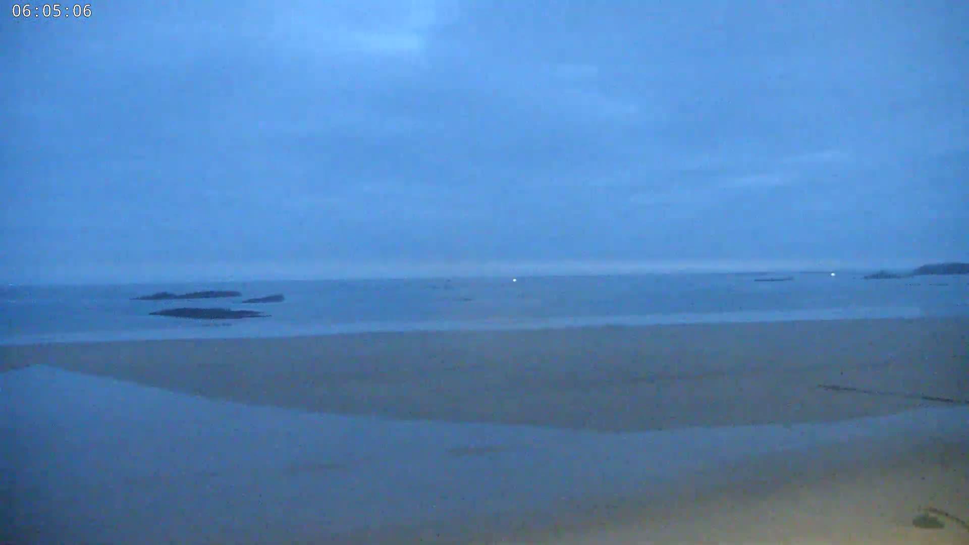 A wide, sandy beach stretches towards a calm, dark blue ocean under a hazy, pre-dawn sky.