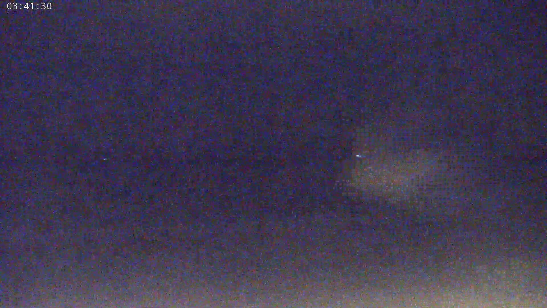 A nighttime image shows a dark sky with a faint, blurry light source in the distance.