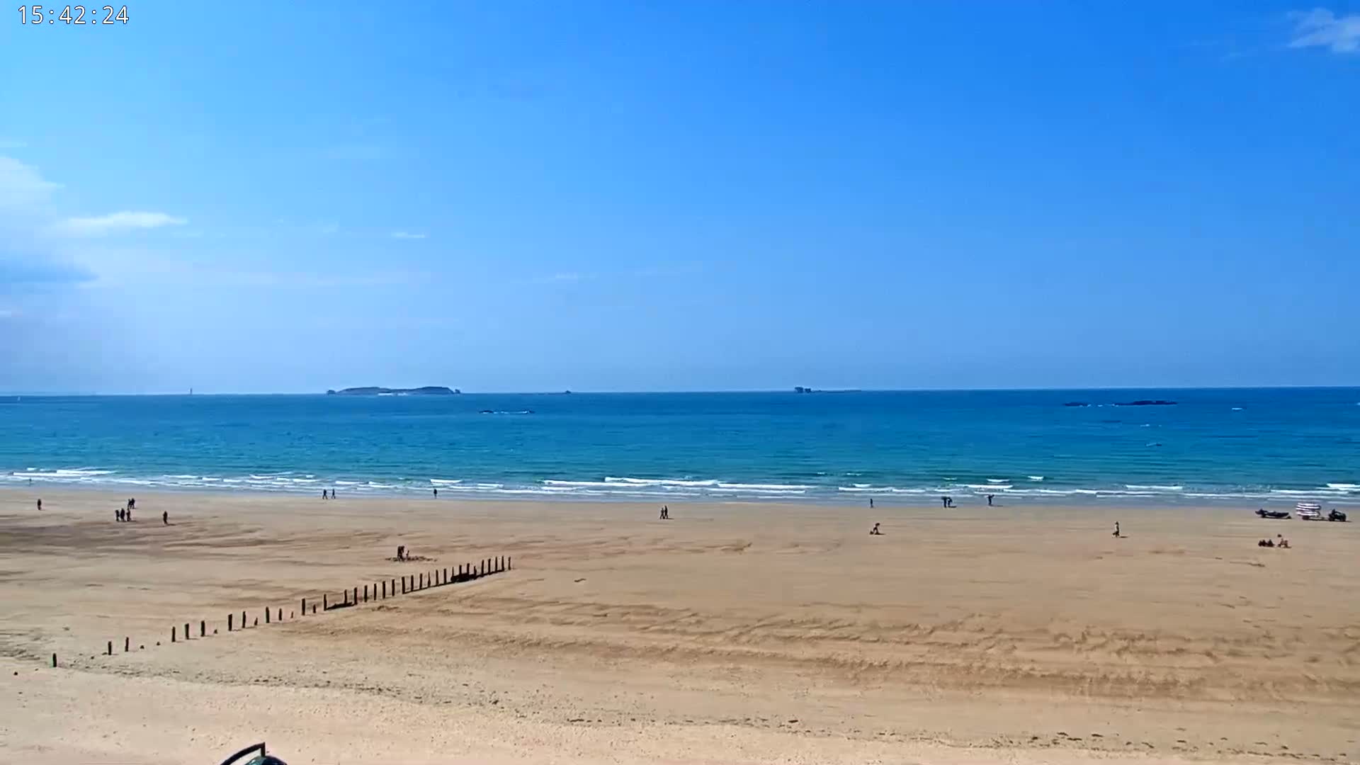 A sandy beach with a few people on it stretches to a calm, turquoise ocean under a clear blue sky.