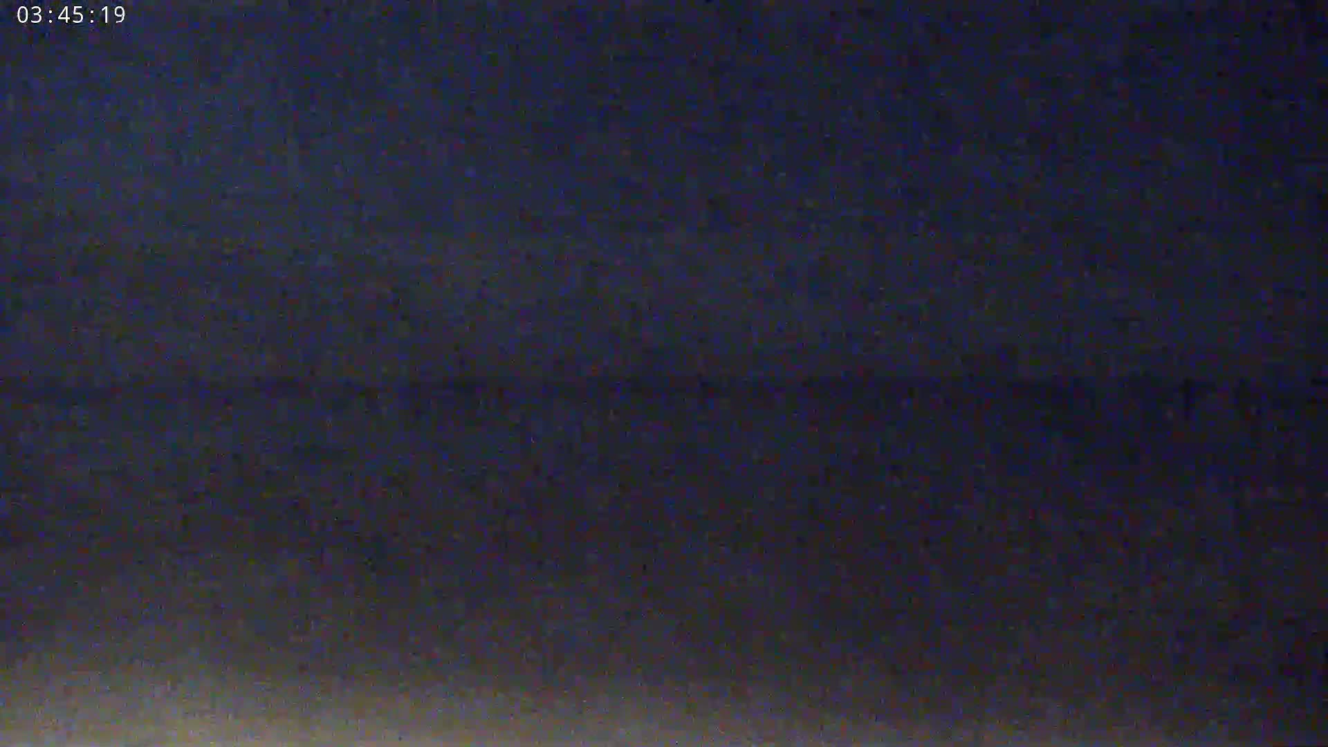 A dark, blurry image shows a mostly dark sky at night with a very faint horizon line.