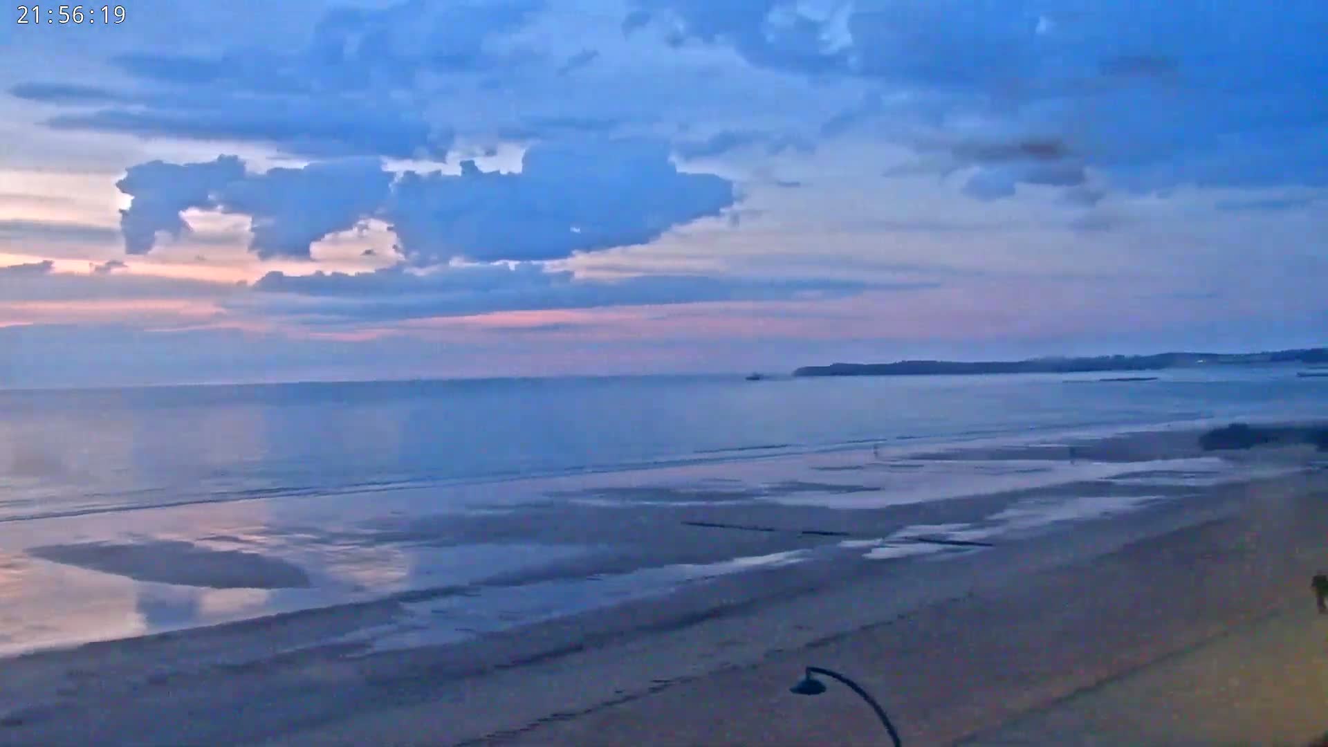 A mostly cloudy, twilight sky over a calm ocean and wide, sandy beach.
