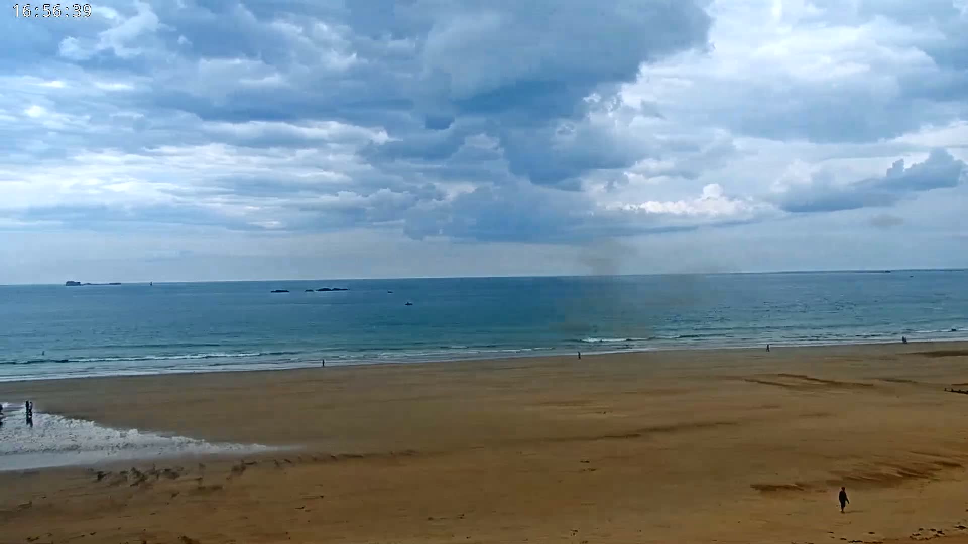 A wide sandy beach stretches towards a calm ocean under a partly cloudy sky.