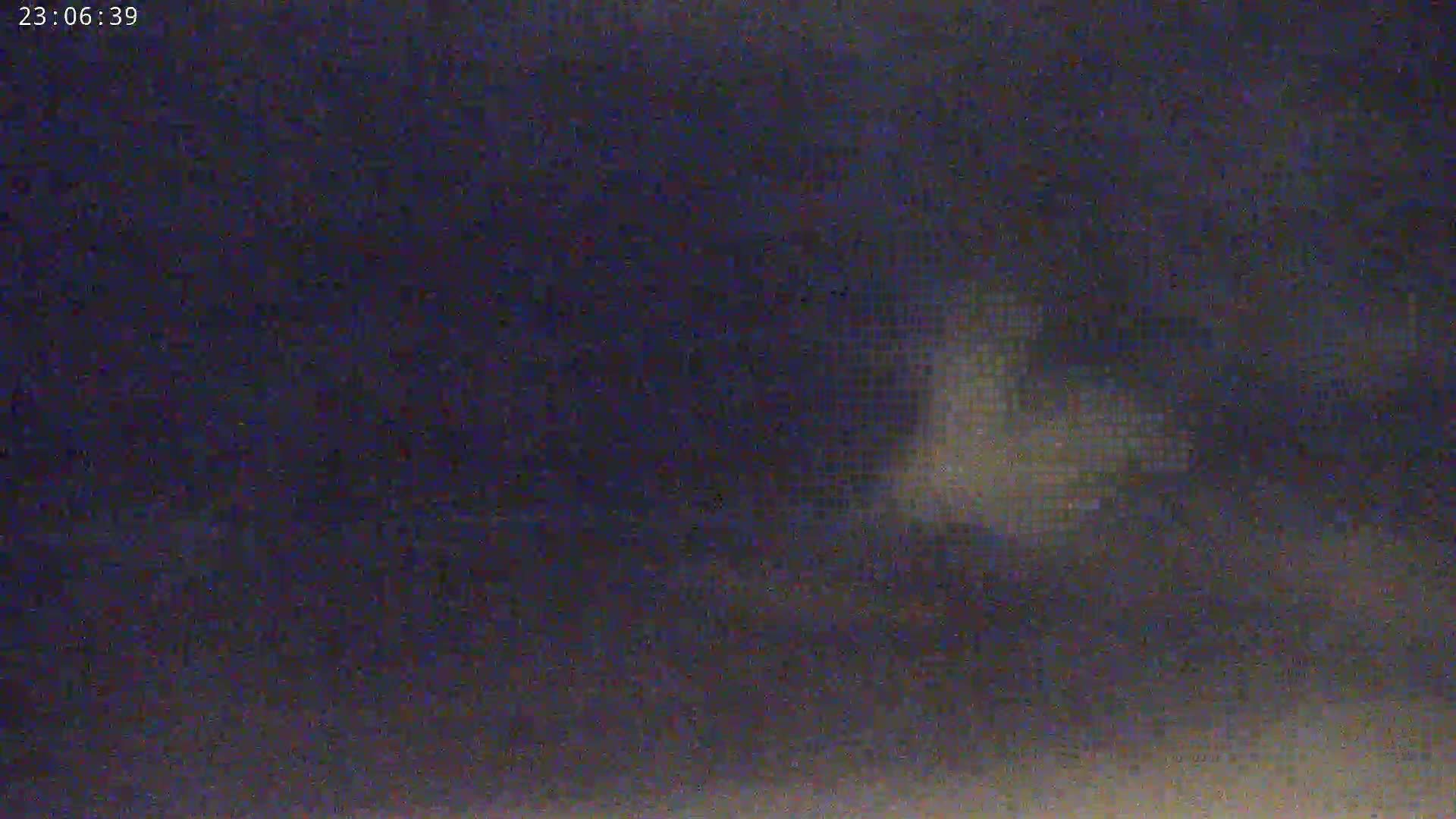 A blurry, dark image shows a faintly illuminated area in the center against a mostly dark background at night.