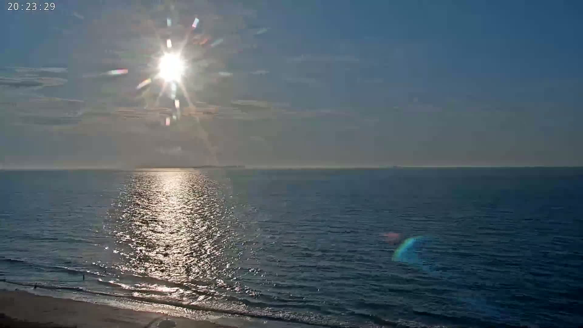 A bright sun shines over a calm ocean meeting a sandy beach.