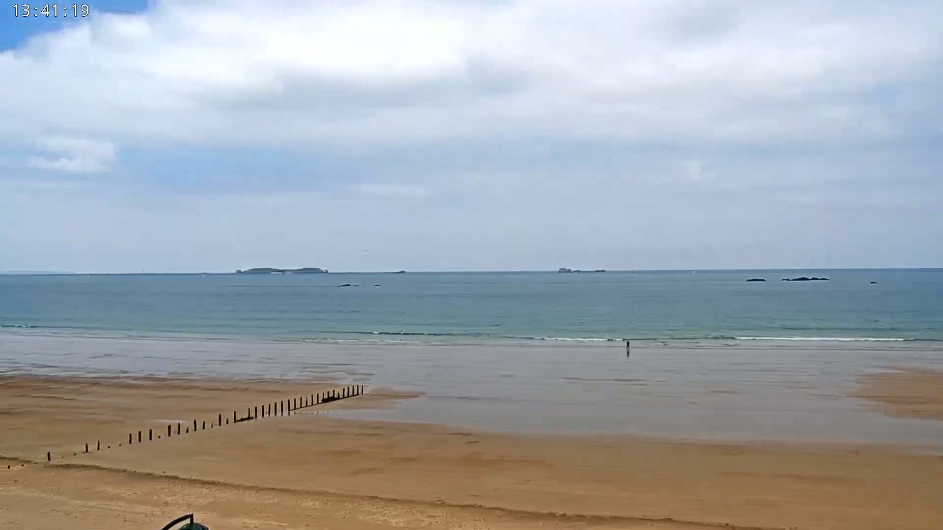 A sandy beach stretches to a calm ocean under a mostly cloudy sky.