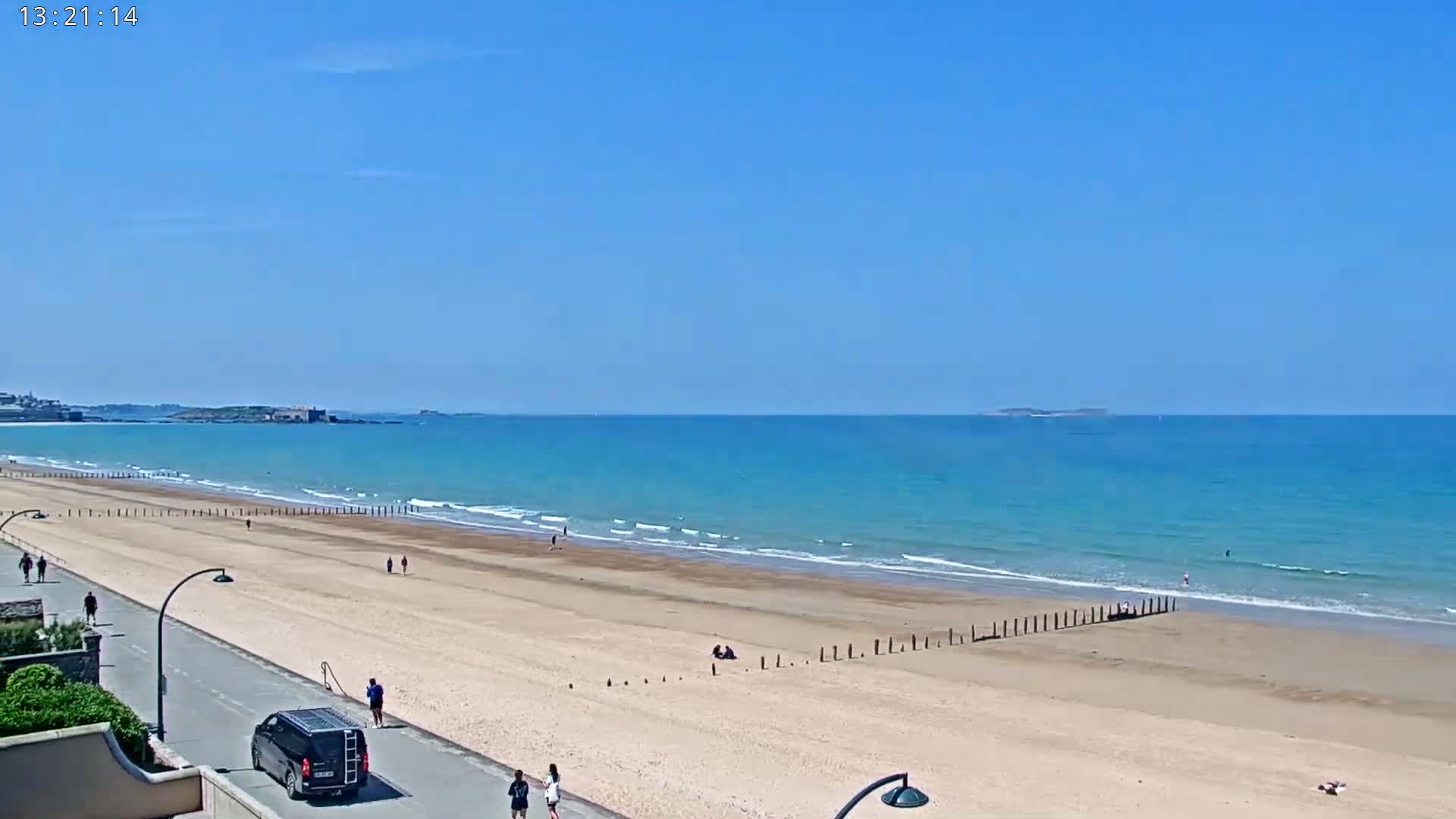 A sandy beach with a few people on it stretches along a turquoise ocean under a clear blue sky.