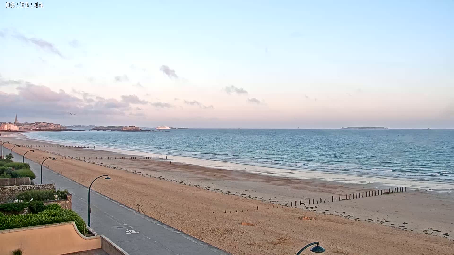 A long sandy beach stretches towards a calm ocean under a pale sunrise sky.