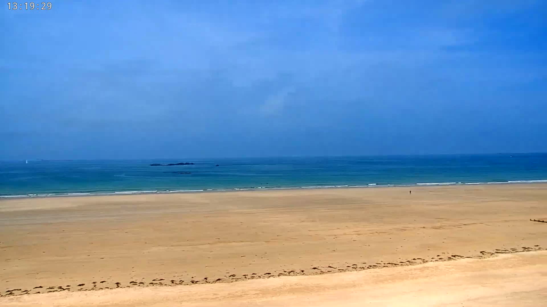 A wide expanse of sandy beach stretches to a calm, blue ocean under a mostly clear sky.